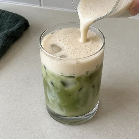 Maple cold foam being poured onto a glass of iced matcha