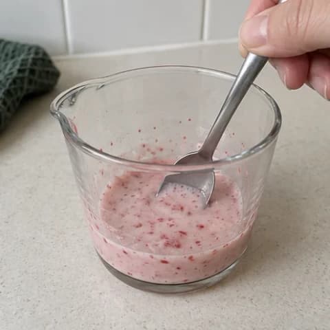 A spoon stirring strawberry powder into a small glass cup of milk