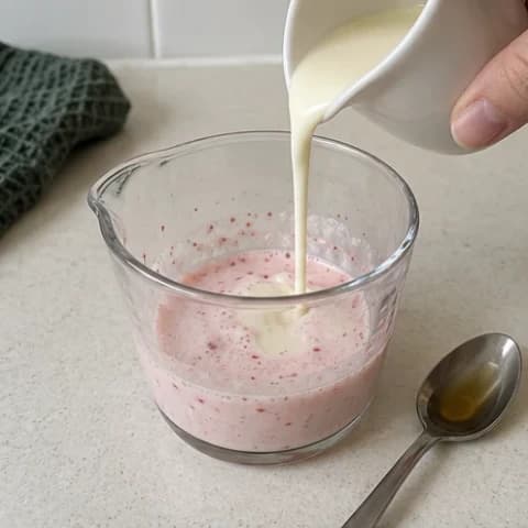 Cream being added to the pink strawberry milk mixture
