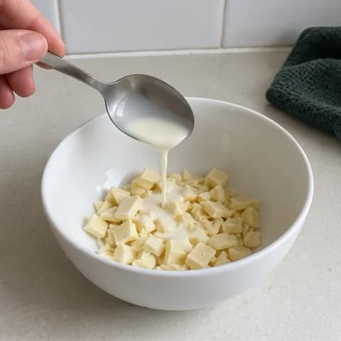 Chopped white chocolate and cream in a small white bowl, ready to melt