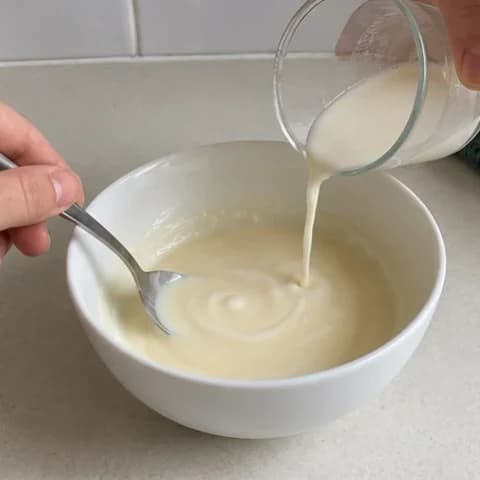A spoon stirring milk and cream into the melted white chocolate mixture