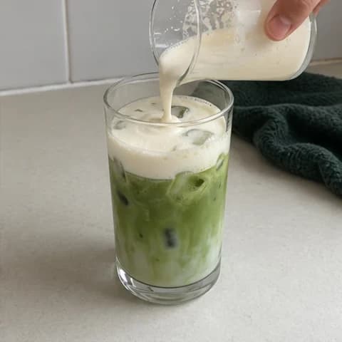 White chocolate cold foam being poured over a green iced matcha latte