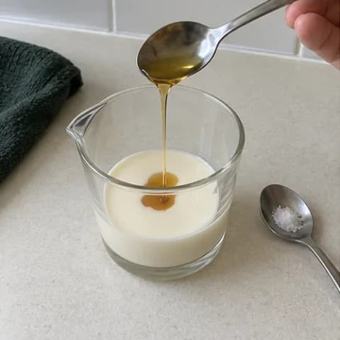 Maple syrup being added to cold cream and milk, with salt beside the cup